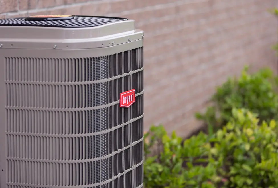 Close-up of an air conditioner unit outside a residential home showing the AC condenser and compressor components, illustrating the difference between AC condenser vs. compressor. Expert AC repair, installation, and maintenance services by Lochard HVAC, Plumbing, and Service. Call today for help with what is an AC condenser vs. compressor, difference between AC condenser and compressor, AC condenser function, AC compressor function, AC condenser repair, AC compressor repair, air conditioner condenser vs compressor, signs of bad AC condenser, signs of faulty AC compressor, AC condenser replacement cost, AC compressor replacement cost, HVAC condenser and compressor service, air conditioning repair near me, AC repair near me, HVAC installation near me, residential AC service, commercial AC repair, emergency AC repair, Lochard HVAC, Plumbing, and Service AC repair, air conditioning maintenance near me, AC unit parts explained, HVAC technician near me, affordable AC repair services.